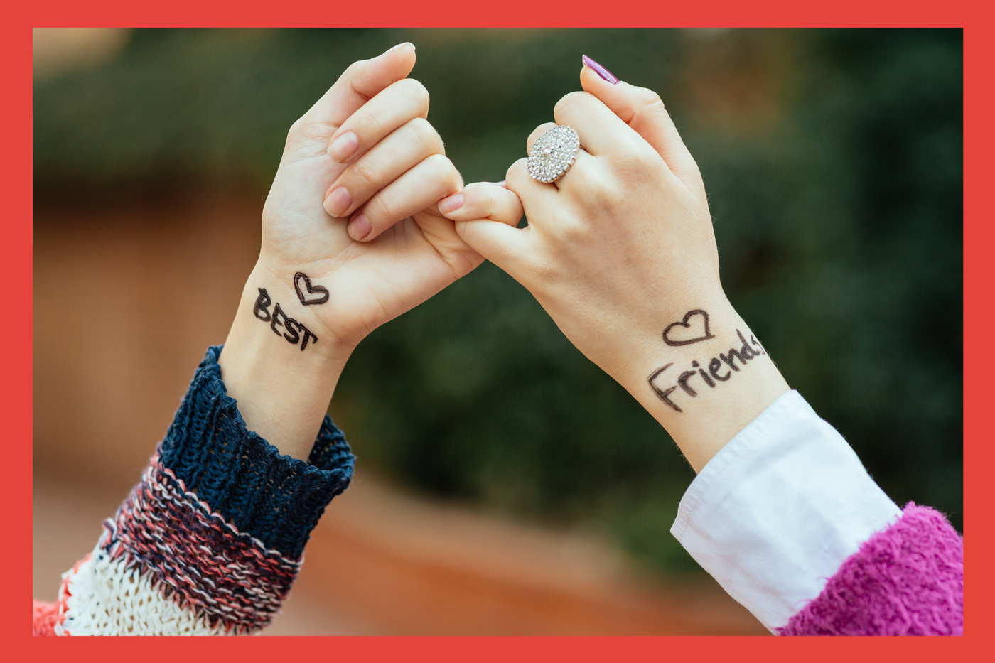 Women making a pinky promise with the words best and friends written on their hands. 